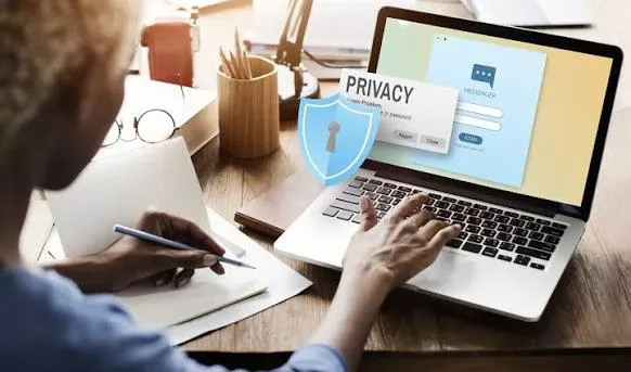 A person taking notes beside a laptop displaying a privacy and cookie consent dialog